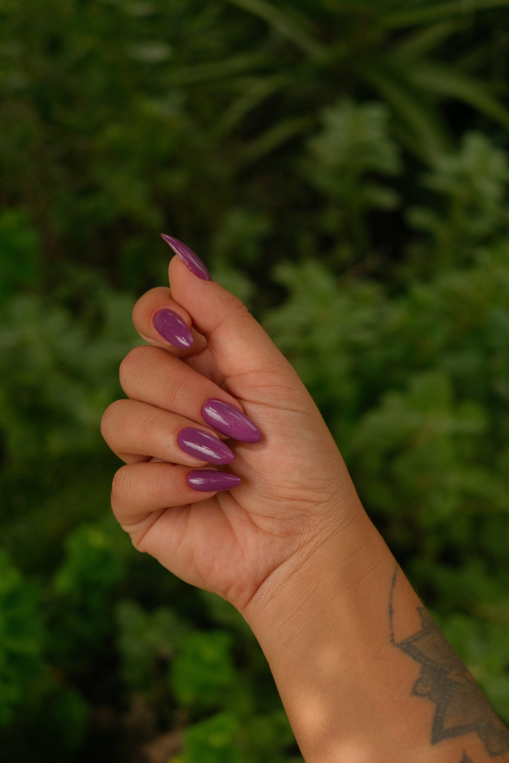 Glossy purple almond nails against green leaves