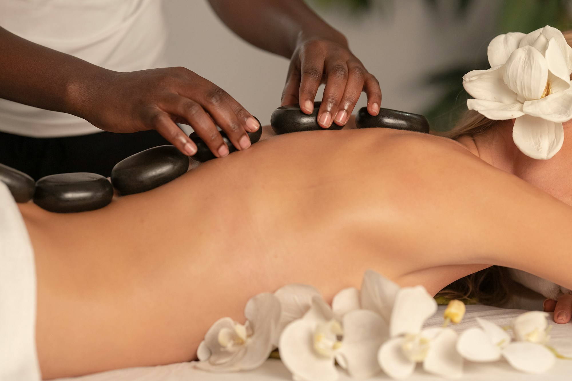 Hot stones placed along a client’s back beside white flowers