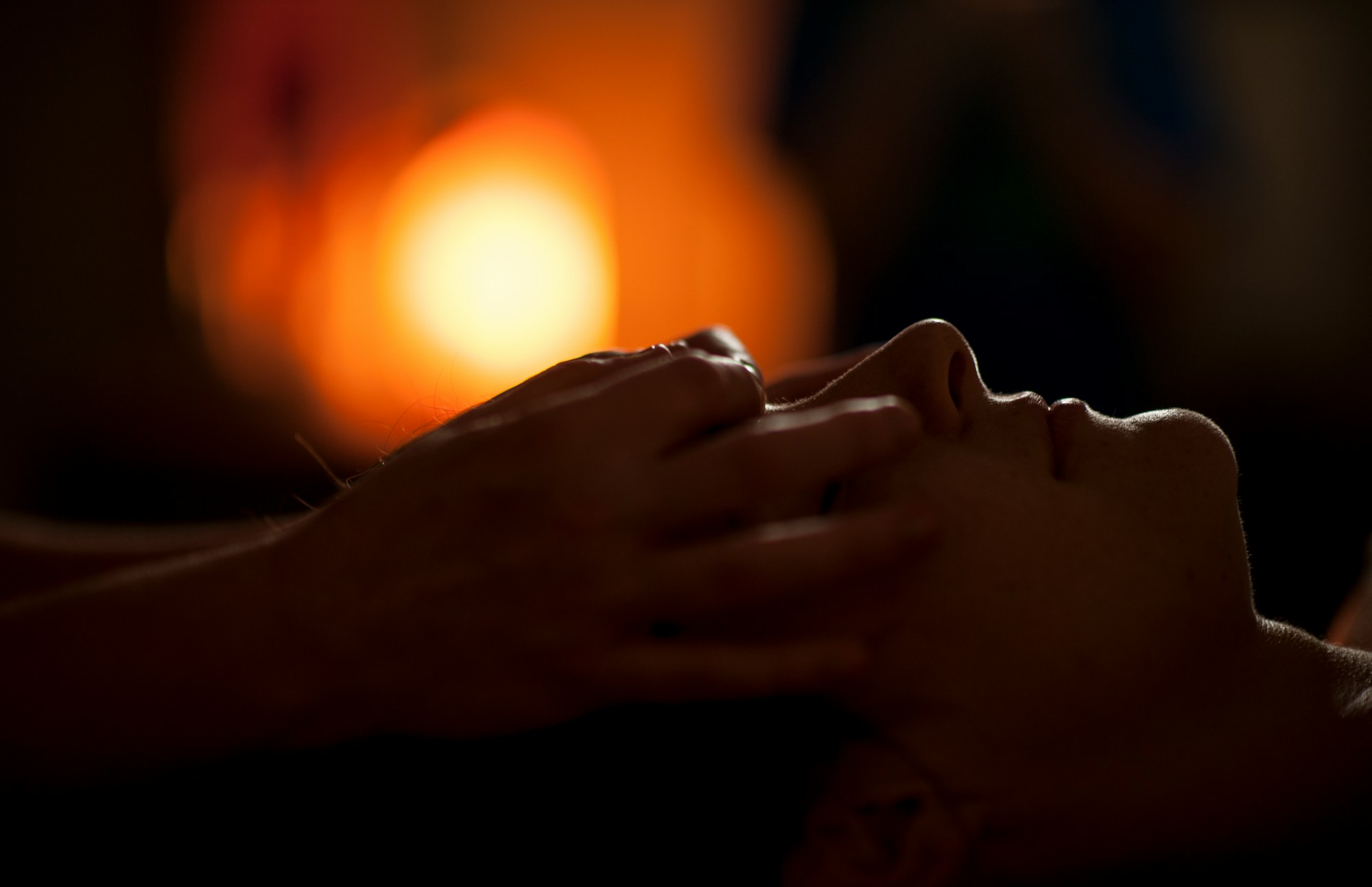 Hands massaging a client’s face in warm candlelight