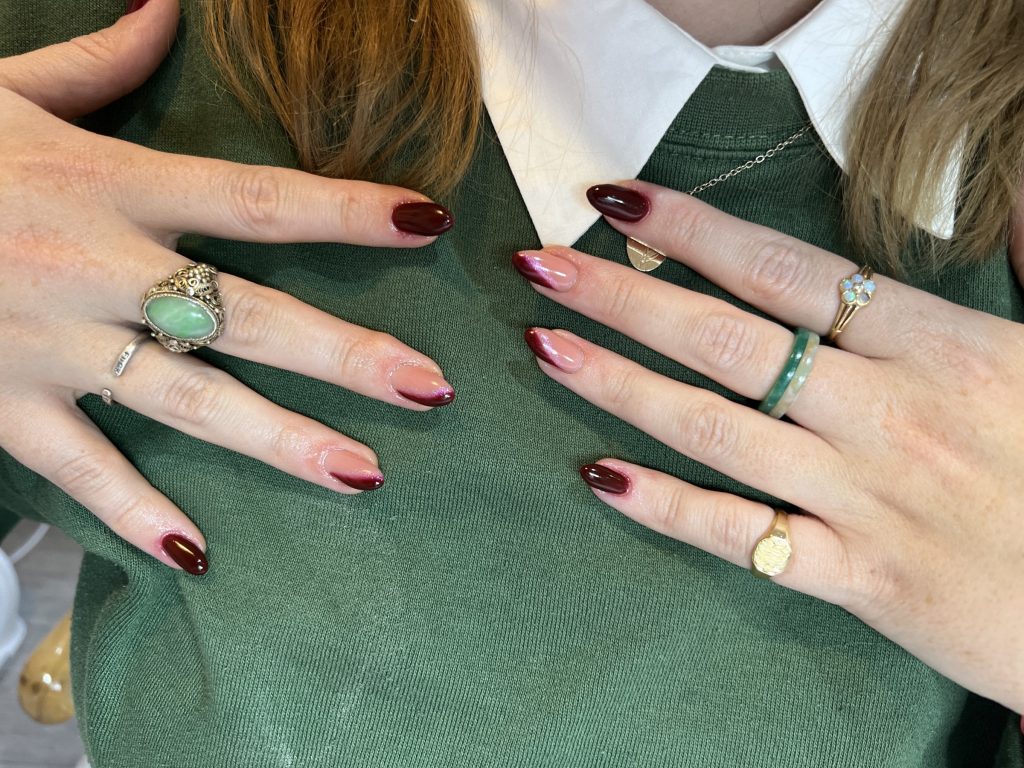 Almond nails in deep burgundy and burgundy French tips, worn with gold rings